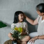 Happy Asian woman caressing charming granddaughter with green plant in pot spending time at home