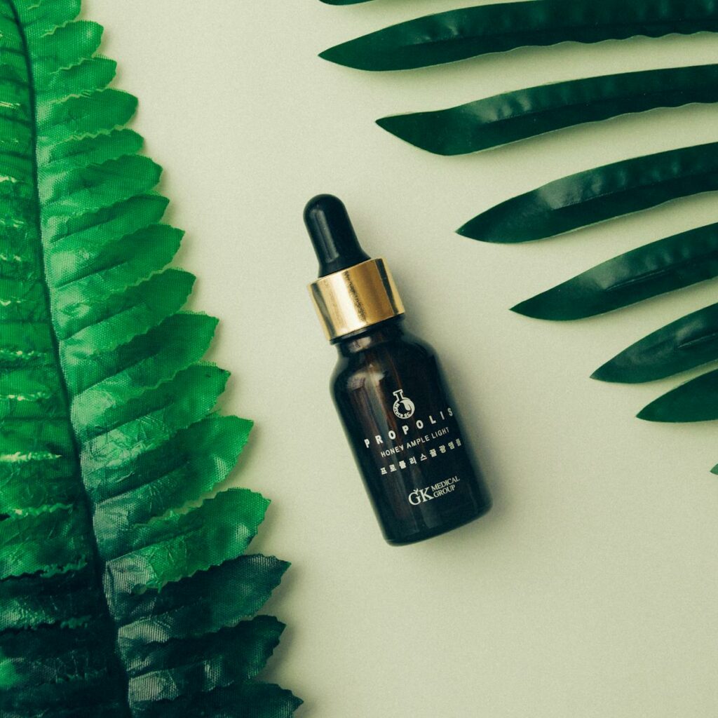 Cosmetic bottle placed near fresh green leaves