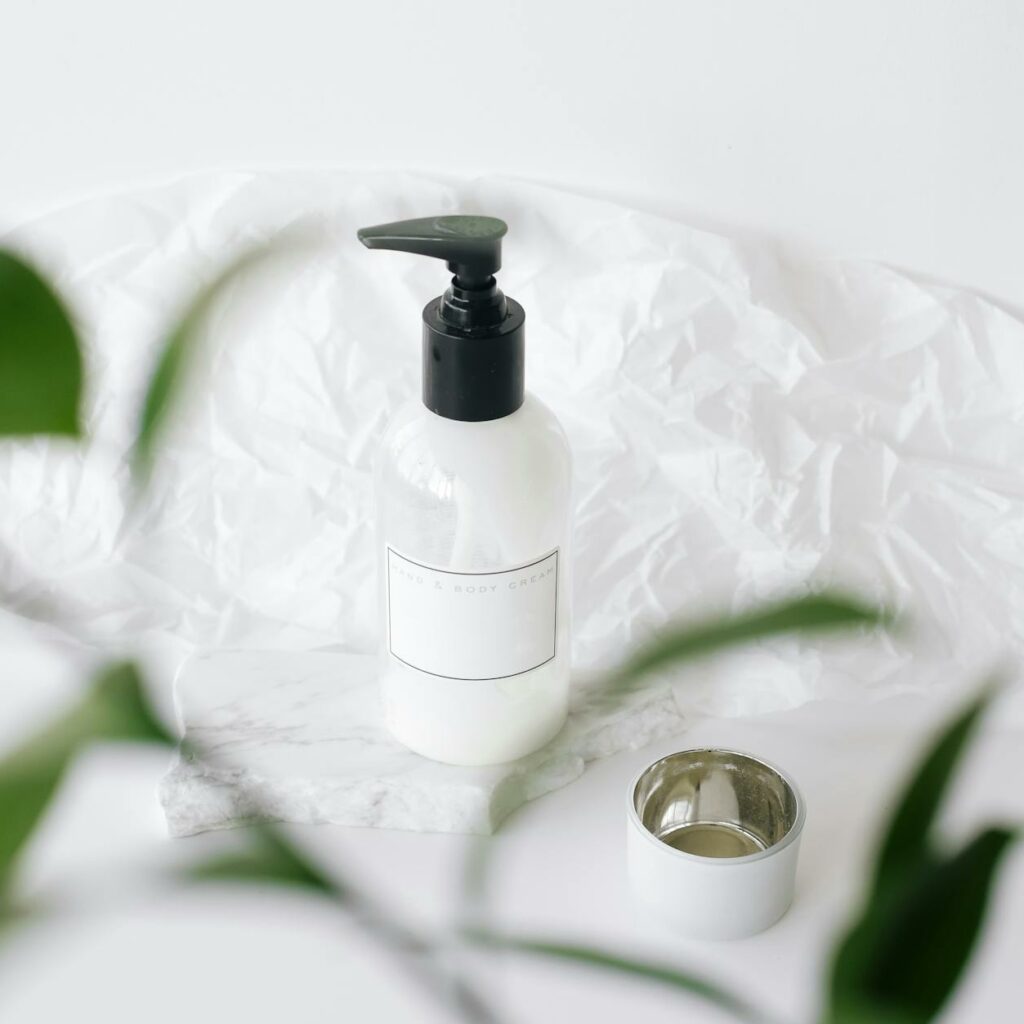 High angle through plant leaves view of plastic bottle with moisturizing lotion placed on white table