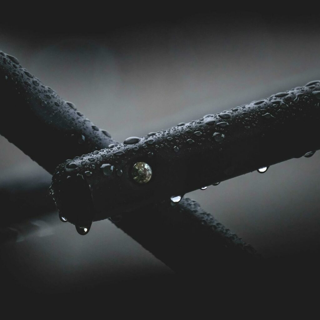 Closeup of black metal pipes covered in water drops and attached with nail