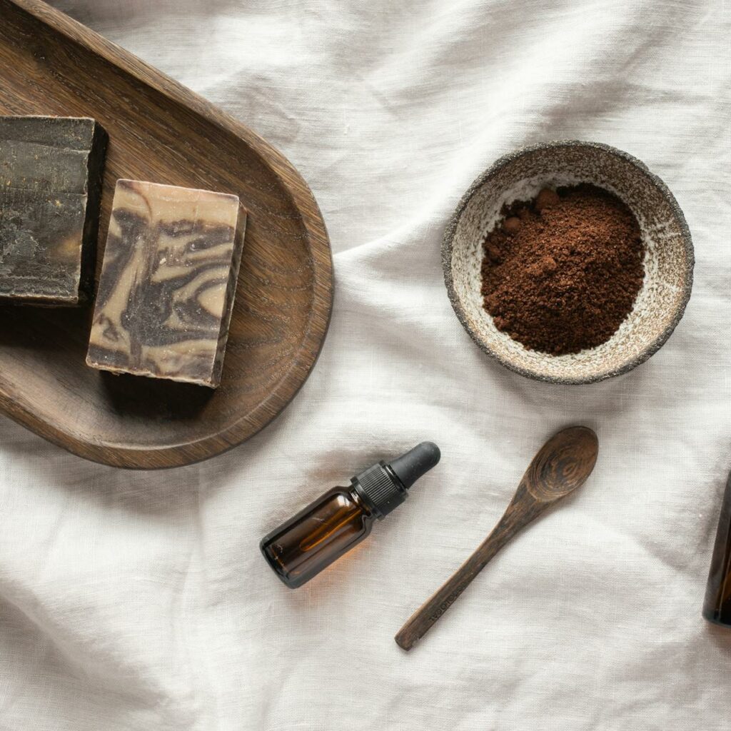 Top view of coffee scrub in bowl composed with bottles of aromatic oil on white sheet