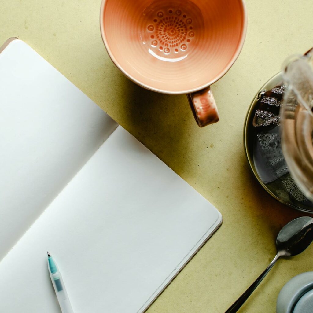 A Blank Notebook Beside Empty Cup and Coffee Maker